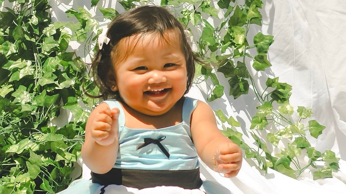 Sky is registered to the contest to win money with this photo: adaptation, baby_toddler_clothing, botany, cheek, chin, facial_expression, finger, gesture, grass, hairstyle, hand, happy, leaf, mouth, people_in_nature, person, plant, skin, smile, thumb