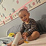 toddler, child, smiling, laughing, striped_shirt, bed, sock, foot, hand, wall, calligraphy, asian_characters, led_light, pajamas, blanket, couch, indoors, happy, person, playing