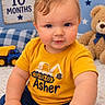 baby, child, infant, portrait, sitting, smiling, blue_eyes, blond_hair, yellow_shirt, construction_shirt, toy_truck, teddy_bear, playroom, indoor, carpet, cushion, stars, blue_background, birthday_milestone, close_up
