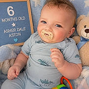 Asher is registered to the contest to win money with this photo: baby, pacifier, plush_toy, blanket, milestone_board, blue_clothing, smiling, cute, indoor, child, star_pattern, toy, infant, portrait, cute_baby, sitting, happy, face, hand, young_child