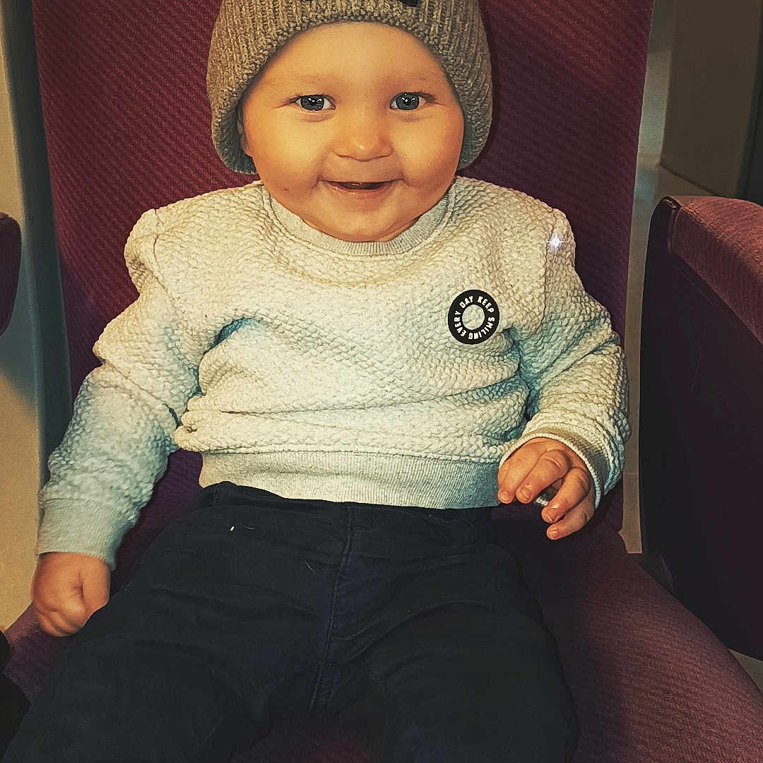 Kaëlan participe au concours pour gagner de l'argent avec cette photo : baby, casual, chair, child, clothing, cozy, cute, face, happy, hat, indoor, knit_hat, pants, person, portrait, seated, smiling, sweater, toddler, warm_lighting