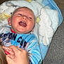 baby, child, laughing, blanket, blue_blanket, hand, wristband, cozy, indoor, carpet, wooden_floor, person, smiling, cute, happy, clothing, face, skin, expression, comfort