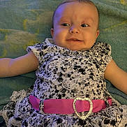 Mary is registered to the contest to win money with this photo: baby, child, infant, dress, floral_pattern, pink_belt, heart_buckle, blanket, lying_down, cute, portrait, face, smile, young_child, fashion, clothing, indoors, soft_texture, happy, person