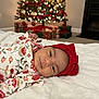 baby, infant, red_bow, headband, floral_clothing, blanket, christmas_tree, decorations, presents, holiday, indoors, soft_texture, cute, smile, face, person, festive, warm, cozy, celebration