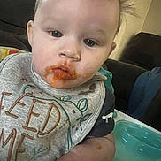 Ashton is registered to the contest to win money with this photo: baby, child, face, food, messy, bib, high_chair, indoor, person, clothing, sitting, curious, mess, feeding, young_child, mouth, hand, furniture, expression, cute