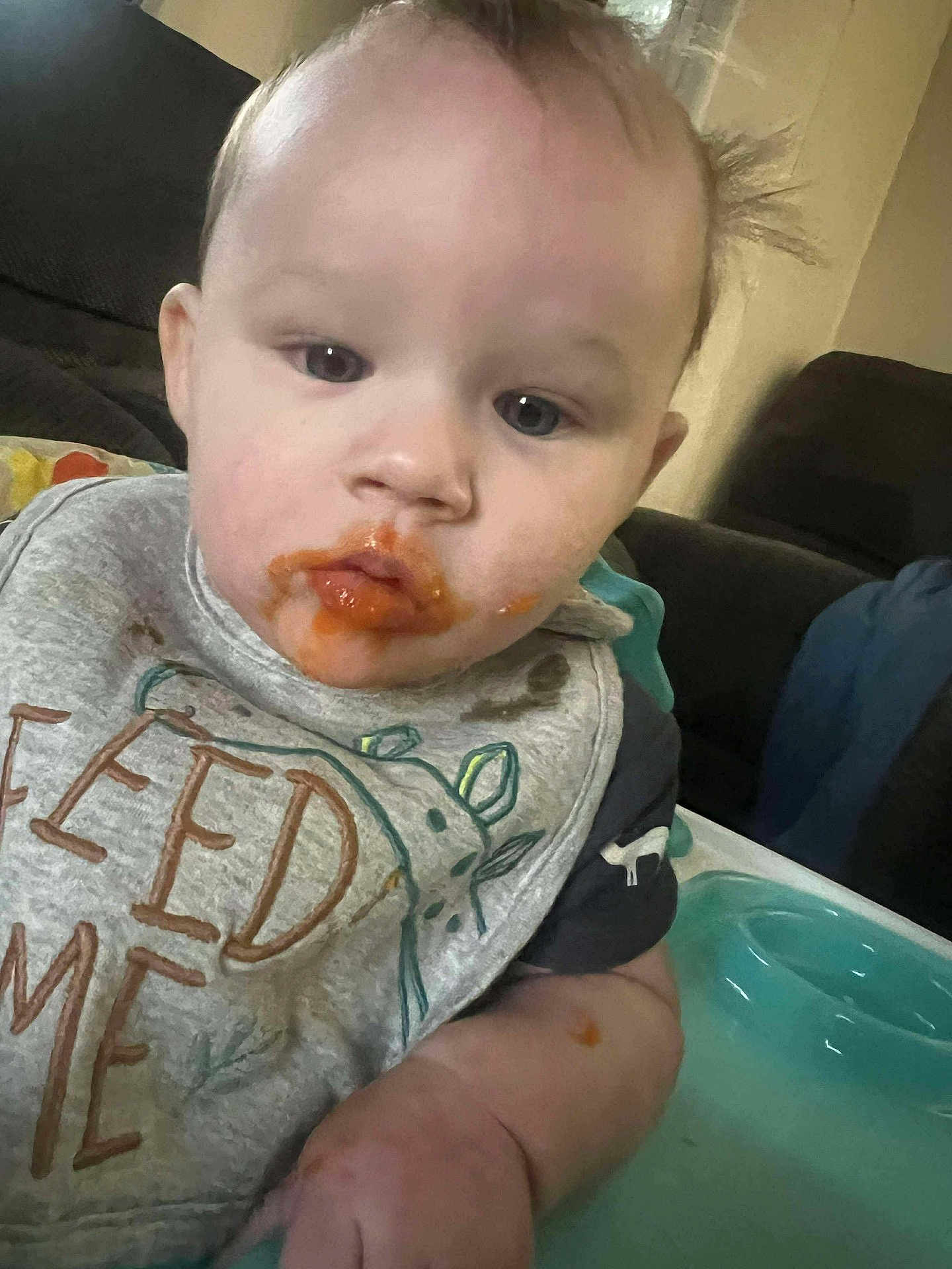 Ashton is registered to the contest to win money with this photo: baby, child, face, food, messy, bib, high_chair, indoor, person, clothing, sitting, curious, mess, feeding, young_child, mouth, hand, furniture, expression, cute