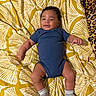 baby, blanket, blue_onesie, child, cute, face, happy, indoors, infant, lying_down, patterned_blanket, relaxed, skin, small_feet, small_hands, smiling, socks, soft_texture, white, yellow