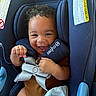 baby, child, car_seat, smiling, curly_hair, safety_straps, blue, infant, cute, happy, seat_belt, clothing, hands, face, portrait, indoor, person, baby_carrier, seat, infant_clothing
