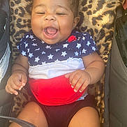 Kya is registered to the contest to win money with this photo: baby, child, smiling, laughing, infant, star_pattern, red_white_blue, leopard_print, cushion, seat, cute, happy, portrait, clothing, skin, hand, legs, indoor, young, person