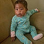 baby, child, onesie, turquoise, floral_pattern, couch, furniture, indoor, curious, sitting, hand, face, expression, person, infant, young_child, home, relaxed, casual, comfortable
