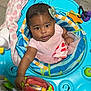 Kya is registered to the contest to win money with this photo: baby, child, infant, activity_center, toy, pink_dress, green_bow, blanket, floor, indoor, cute, smiling, playful, colorful, blue, person, young, happy, seated, curious