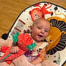 baby, infant, blanket, plush_toy, pacifier, baby_seat, lion_print, monkey_print, flooring, wood_floor, child, smiling, happy, indoors, cute, person, soft_texture, colorful, comfort, toy