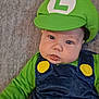 baby, child, costume, green_hat, luigi, blue_overalls, yellow_buttons, face, cheeks, eyes, mouth, clothing, infant, portrait, cute, lying_down, soft_texture, indoor, person, headwear