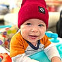 baby, child, smiling, red_hat, knit_hat, toy, indoor, happy, face, cute, infant, clothing, colorful, playtime, hands, portrait, closeup, expression, sitting, bright