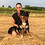 animal, black_fur, brown_fur, canine, dog, field, glasses, grass, happy, hay_bale, nature, outdoor, person, pet, rural, scenery, smile, summer, sunlight, white_fur