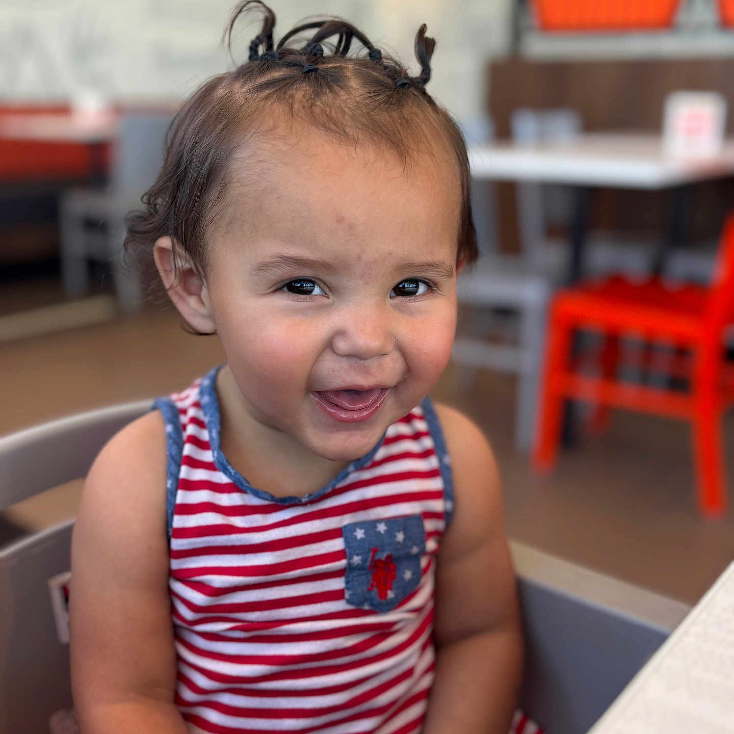 Zareya joined the competition — help win amazing prizes! baby, casual, chair, child, cute, face, fun, hair, happy, high_chair, indoor, person, pigtails, portrait, restaurant, seated, smiling, striped_dress, table, toddler