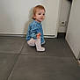 baby, candid, casual_clothing, child, curious, denim_shirt, door, floor_tile, footwear, hair, indoor, light_pants, long_sleeve, person, plug_socket, squatting, tiled_floor, toddler, wall, young_child