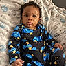 baby, child, infant, onesie, clothing, stars, clouds, moon, blue, yellow, blanket, elephant_pattern, fabric, indoor, portrait, face, expression, curly_hair, sitting, person