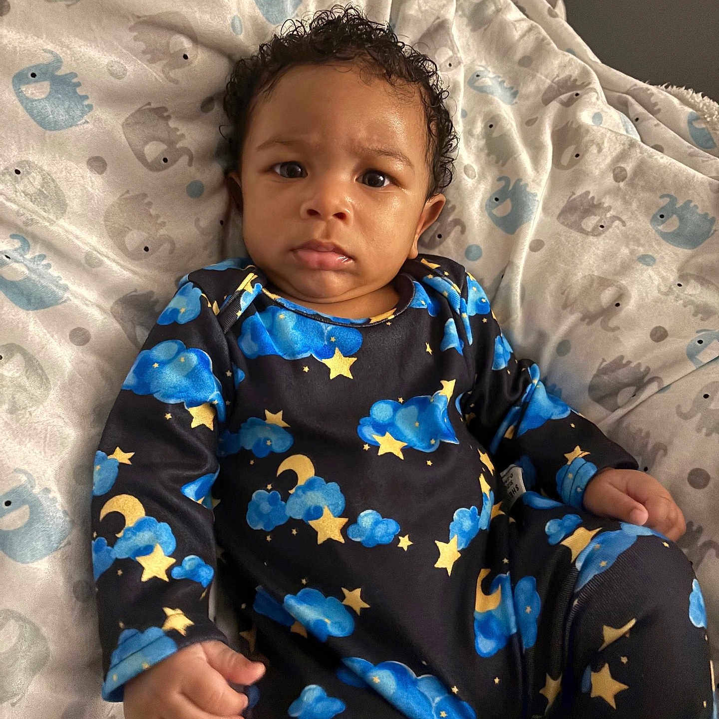 Zyire joined the competition — help win amazing prizes! baby, child, infant, onesie, clothing, stars, clouds, moon, blue, yellow, blanket, elephant_pattern, fabric, indoor, portrait, face, expression, curly_hair, sitting, person