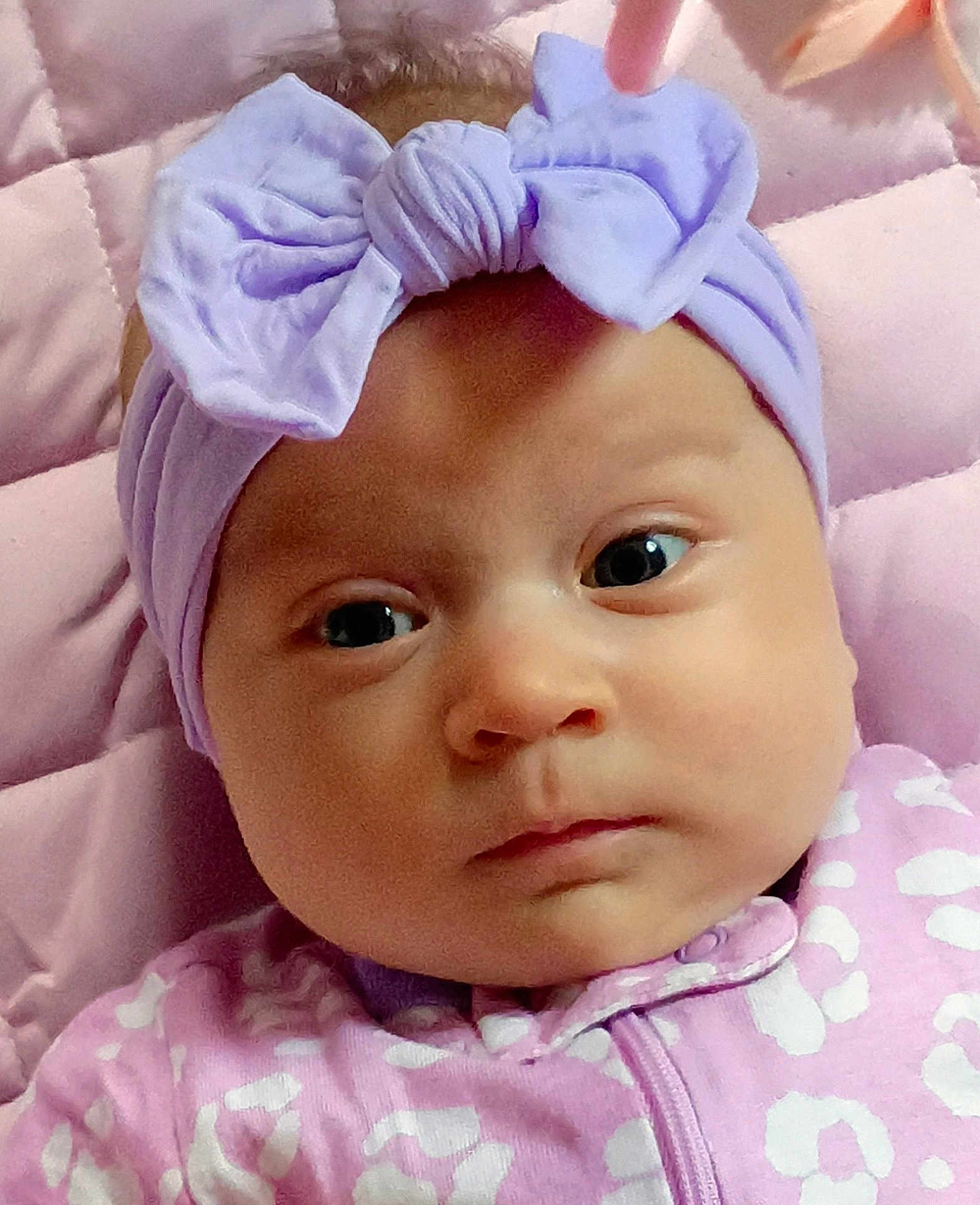 Jayca joined the competition — help win amazing prizes! baby, infant, headband, bow, pink, lavender, onesie, closeup, portrait, face, eyes, soft, quilt, patterned_clothing, child, newborn, cute, expression, laying, indoors