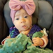 Jayca is registered to the contest to win money with this photo: baby, infant, car_seat, headband, pink_bow, blanket, pacifier, plush_toy, clothing, hand, face, blue_eyes, child, seatbelt, soft_texture, cute, indoors, portrait, expression, young