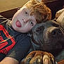 boy, dog, face, tongue, paw, couch, shirt, red, black, hair, closeup, indoor, child, pet, relaxing, friendship, cozy, expression, casual, resting