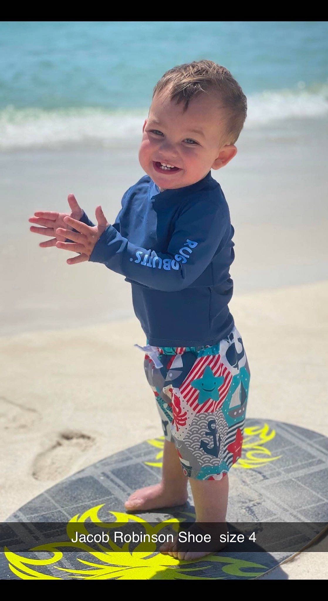 Jacob is registered to the contest to win money with this photo: azure, baby_toddler_clothing, barefoot, beach, board_short, electric_blue, face, fun, happy, head, joy, leisure, people_on_beach, person, sand, sleeve, smile, summer, surfboard, t_shirt