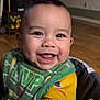 baby, smiling, face, dimples, indoor, child, clothing, bib, yellow_shirt, happy, portrait, person, cheerful, young_child, cute, closeup, seat, wooden_floor, background_blur, expression