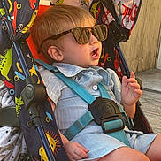Fletcher is registered to the contest to win money with this photo: animal_print, baby, baby_stroller, casual, child, clothing, colorful, cute, expression, outdoor, person, playful, seat, seatbelt, stroller, summer, sunglasses, sunlight, toddler, wooden_deck