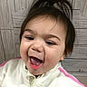 Rynlee joined the competition — help win amazing prizes! child, toddler, baby, portrait, smiling, laughing, happy, face, open_mouth, dark_hair, ponytails, indoors, close_up, sporty_clothing, white_clothing, pink_accents, wood_background, seated, joyful, photography