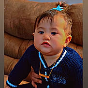 Akaialoha is registered to the contest to win money with this photo: baby, blue_sweater, child, chubby_cheeks, clothing, couch, cute, face, hair_bow, hand, holding, home, indoor, looking_at_camera, necklace, person, portrait, seated, toddler, young_child
