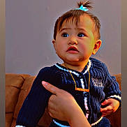 Akaialoha joined the competition — help win amazing prizes! baby, child, person, face, hand, hair_tie, sweater, blue, navy, couch, indoor, portrait, expression, curious, young_child, skin, necklace, seated, supporting_hand, closeup