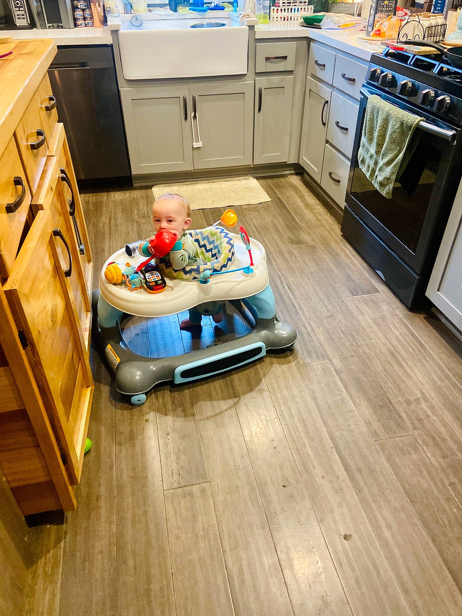 Colton is registered to the contest to win money with this photo: cabinetry, chest_of_drawers, countertop, drawer, floor, flooring, furniture, gas_stove, hardwood, interior_design, kitchen, kitchen_appliance, laminate_flooring, living_room, person, refrigerator, table, toddler, varnish, wood