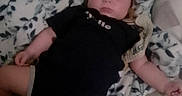 John is registered to the contest to win money with this photo: baby, infant, sleeping, face, portrait, black_outfit, blanket, bed, bedding, patterned_fabric, leaf_pattern, indoors, lying_down, arms, legs, peaceful, cozy, home, photograph, timestamp