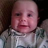 John is registered to the contest to win money with this photo: baby, child, infant, portrait, face, eyes, looking_at_camera, neutral_expression, seated, couch, sofa, cushion, indoor, home, clothing, onesie, patterned_clothing, close_up, photograph, date_stamp