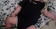 John is registered to the contest to win money with this photo: baby, infant, child, sleeping, portrait, indoors, blanket, bed, onesie, black_clothing, patterned_bedding, lying_down, face, arms, legs, cozy, home, timestamp, low_light, photograph