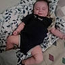 John is registered to the contest to win money with this photo: baby, infant, child, sleeping, portrait, indoors, blanket, bed, onesie, black_clothing, patterned_bedding, lying_down, face, arms, legs, cozy, home, timestamp, low_light, photograph