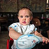 arm, baby, bib, blurred_background, casual, child, clothing, curious, drool, expression, face, high_chair, indoor, light, person, portrait, seat, table, toddler, young_child