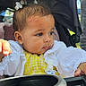 Emilia is registered to the contest to win money with this photo: baby, child, stroller, hair_clips, yellow_outfit, white_jacket, earrings, cup_holder, outdoor, daylight, portrait, infant, curious, face, person, young_child, seated, closeup, expression, cute