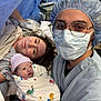 Rosie is registered to the contest to win money with this photo: newborn, baby, mother, hospital, medical_professional, face_mask, hospital_bed, blanket, gown, hat, medical_equipment, smile, patient, indoors, person, portrait, newborn_baby, headwear, healthcare, family
