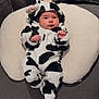 Lara is registered to the contest to win money with this photo: baby, cow_costume, infant, plush, cushion, gray_couch, blanket, baby_clothing, indoor, cute, child, portrait, soft_toys, comfortable, resting, small_hands, face, headwear, seated, cozy