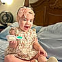 baby, child, smiling, headband, bow, dress, floral, sitting, bed, pillow, brush, footwear, indoors, soft_lighting, happy, person, cute, infant, toy, home