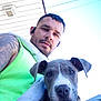 Freya is registered to the contest to win money with this photo: man, dog, puppy, portrait, outdoor, tattoo, tank_top, earbuds, blue_sky, house, roof, pet, animal, person, casual, friendship, close_up, daylight, cute, young_adult