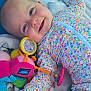 baby, infant, smile, floral_onesie, toy, blanket, colorful, playful, happy, cute, face, child, lying_down, soft_texture, indoors, joyful, cheerful, closeup, person, emotion