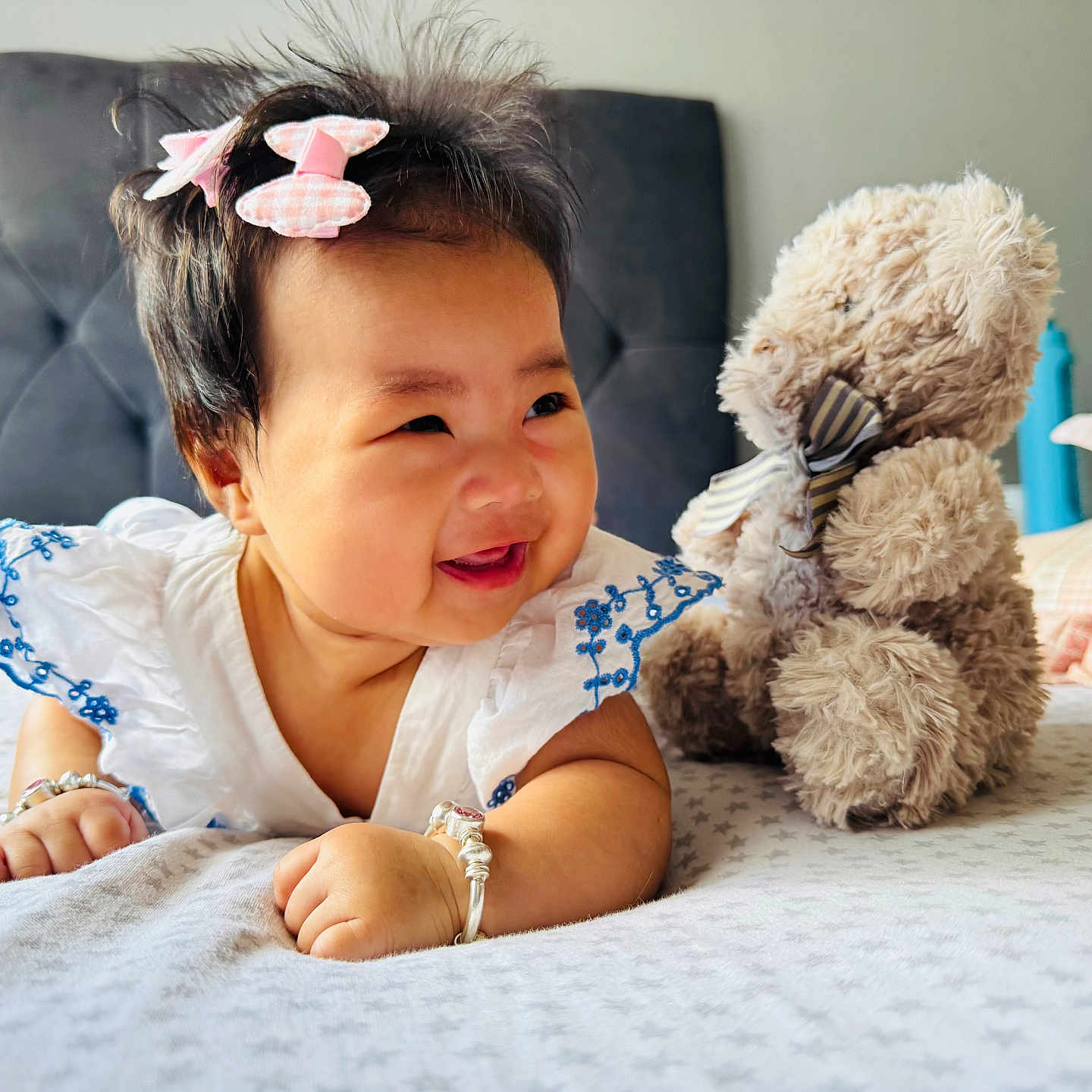 Yulin is registered to the contest to win money with this photo: baby, bed, bracelet, child, cute, embroidered, furniture, hair_bows, happy, headboard, indoor, infant, person, pillow, playful, plush_toy, smiling, soft_toy, teddy_bear, white_dress