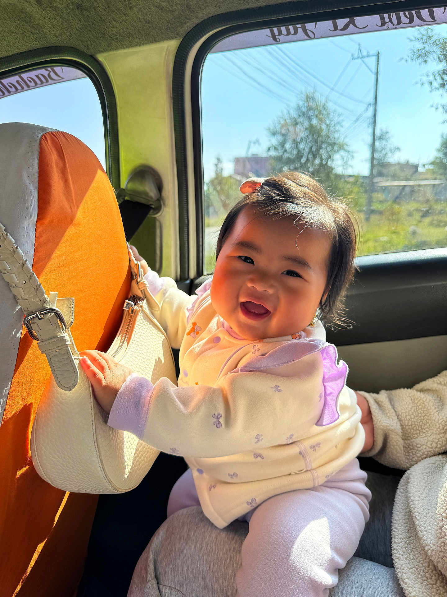 Yulin Fung Tumbapo joined the competition — help win amazing prizes! baby, smiling, car_interior, handbag, orange_seat_cover, window, sunlight, clothing, child, person, face, happy, sitting, cute, infant, jacket, pants, hair, daylight, seatbelt