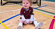 Harrison joined the competition — help win amazing prizes! athletic, child, curly_hair, cute, floor_lines, goalpost, indoor, maroon_shirt, playful, portrait, sitting, smiling, soccer_uniform, sports_court, sports_equipment, toddler, white_shoes, white_shorts, white_socks, young_child