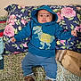 baby, blue_hoodie, dinosaur_print, coolest_brother, floral_pillow, patterned_blanket, brown_shoes, indoor, child, cute, lying_down, clothing, face, person, infant, portrait, casual, expression, small_fists, comfortable