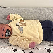 Liam a rejoint le concours — aidez-le/la à gagner de superbes lots ! baby, pacifier, sweater, animal_print, navy_pants, striped_socks, star_pattern, cushion, gray_towel, infant, sleepy, lying_down, indoors, cute, cozy, child, clothing, baby_girl, baby_boy, soft_fabric
