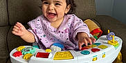 Vanellope is registered to the contest to win money with this photo: baby, child, smile, happy, toy, activity_seat, couch, indoor, foot, hand, clothing, hair_bow, infantino, play, colorful, person, seat, cute, expression, infant